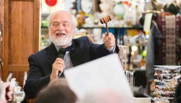 Smiling auctioneer with good for sale behind him.