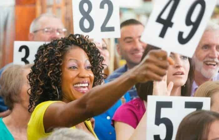 smiling woman in a crowd of people. She is holding an auction number panel.