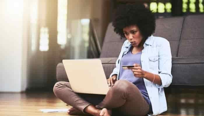 woman sitting on the floor with laptop on her lap and a bank card in her hand