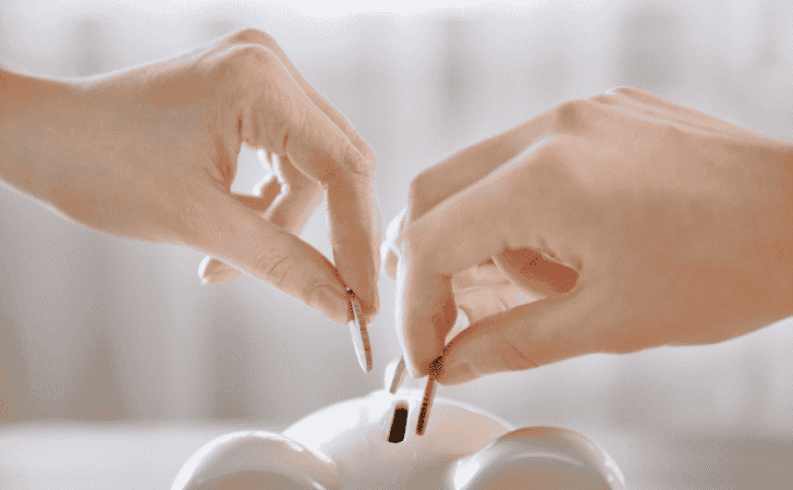 hands putting coins in a piggy bank