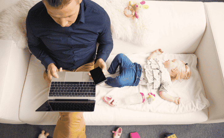 baby sleeping on sofa next to dad with laptop