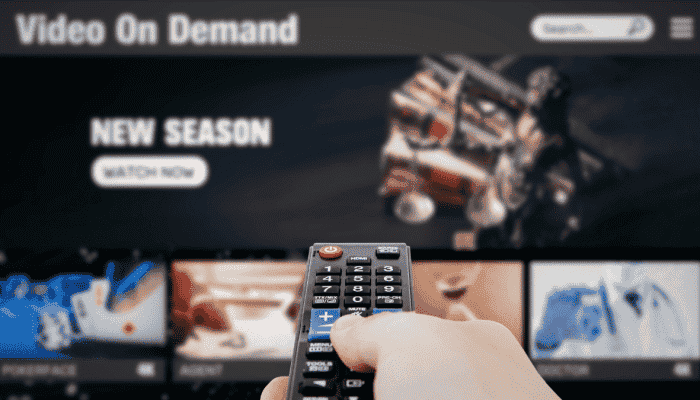 close up of a hand holding a remote control, in front of a blurred TV