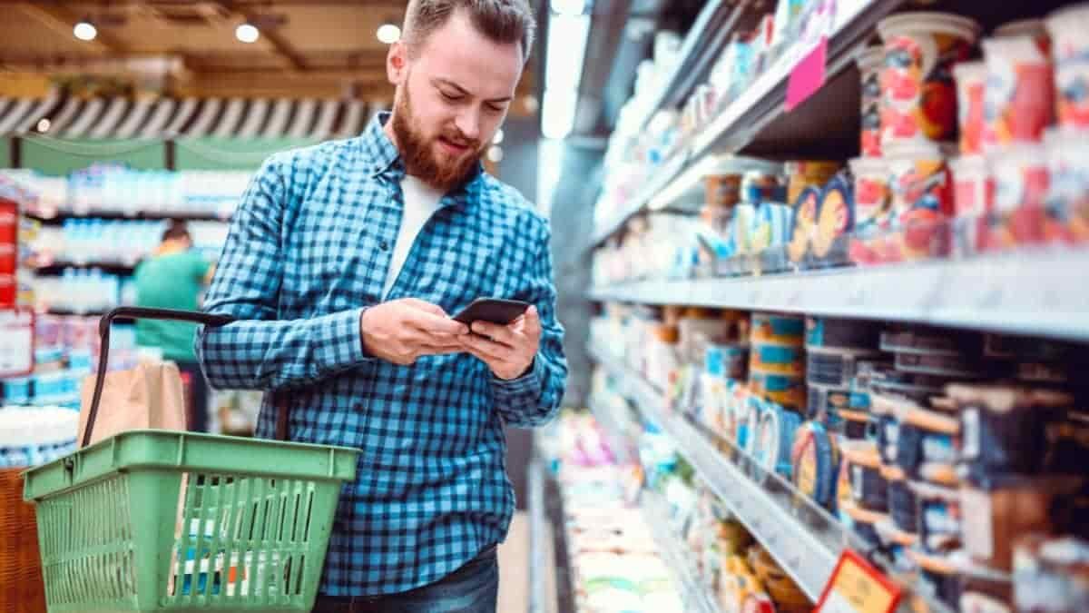 Man in supermarket checking prices on his mobile phone