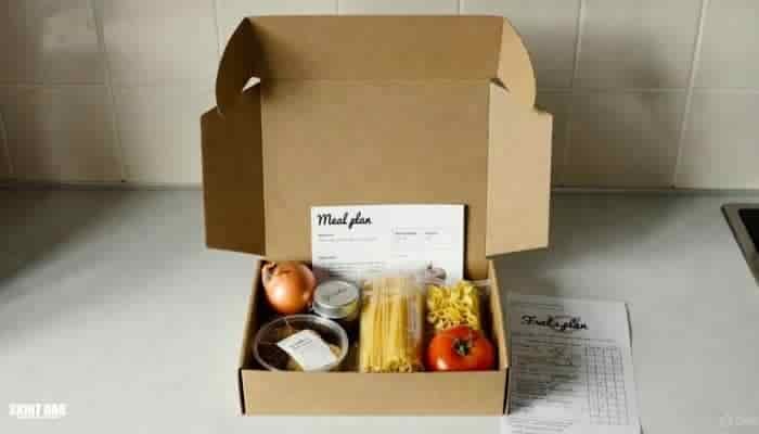 Open meal kit box on a normal UK kitchen worktop with simple ingredients and a recipe card, showing how meal kits can help with meal planning and reducing waste.
