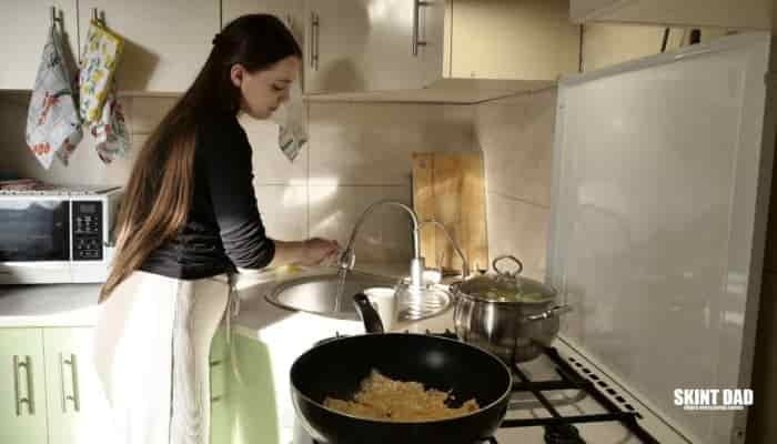 woman washing hands in the sink while food is cooking in pans on the stove.