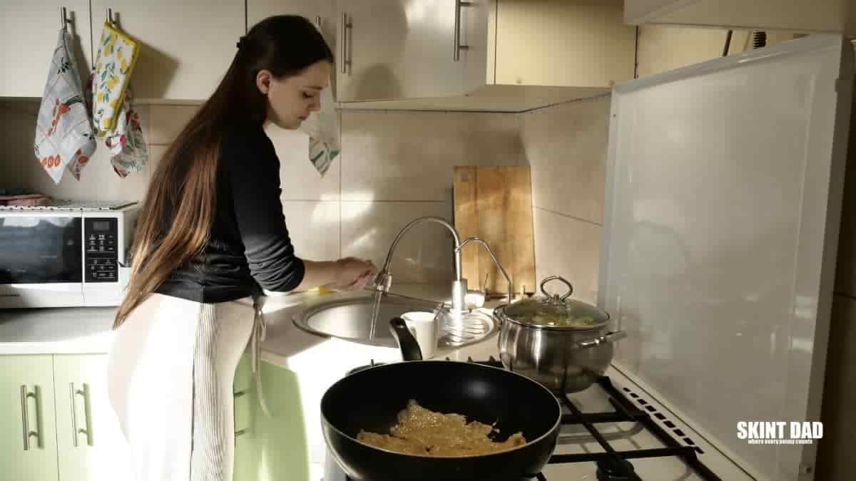 woman washing hands in the sink while food is cooking in pans on the stove.
